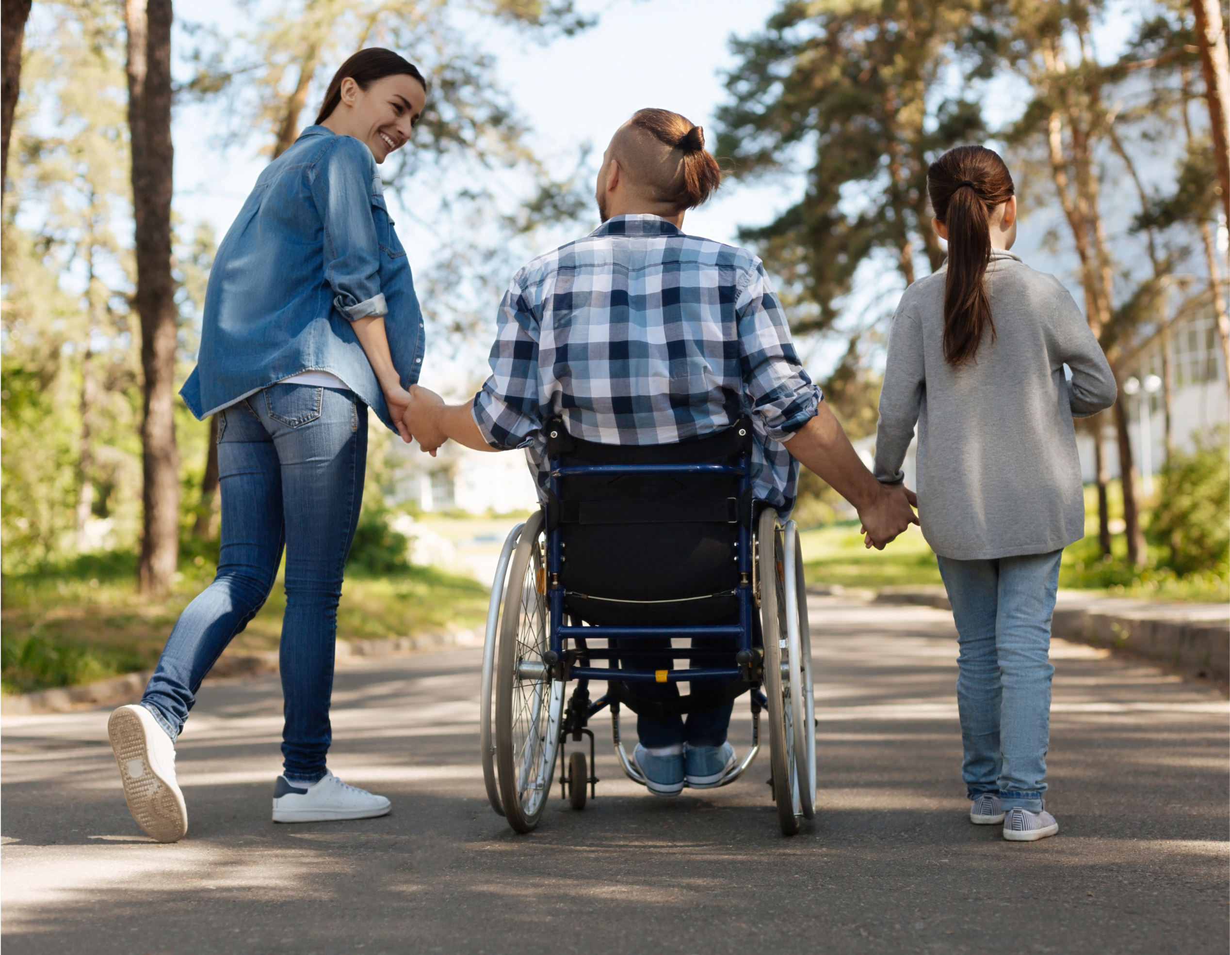 Wheelchair user holding hands with two people while enjoying an outdoor walk, highlighting disability inclusion, accessibility and community participation.